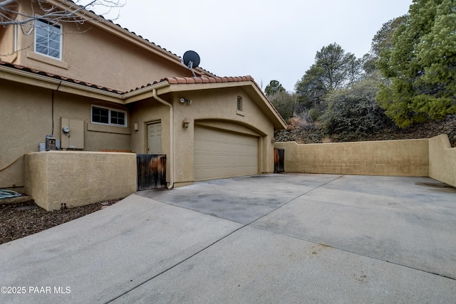 view of home's exterior featuring fence, concrete driveway, a tile roof, stucco siding, and a garage