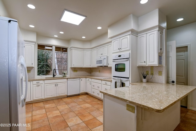 kitchen featuring white appliances, light tile patterned floors, a peninsula, a sink, and white cabinets