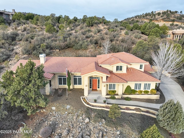 mediterranean / spanish-style home featuring stucco siding, a chimney, and a tile roof