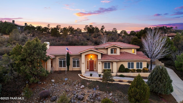 mediterranean / spanish-style home with stucco siding, a tiled roof, and a chimney