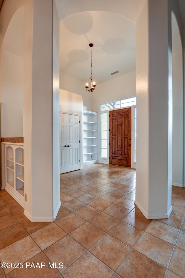 entryway featuring light tile patterned flooring, an inviting chandelier, and baseboards