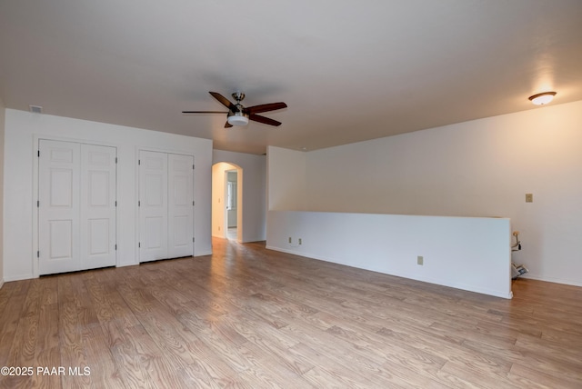 interior space with visible vents, baseboards, ceiling fan, light wood-type flooring, and arched walkways