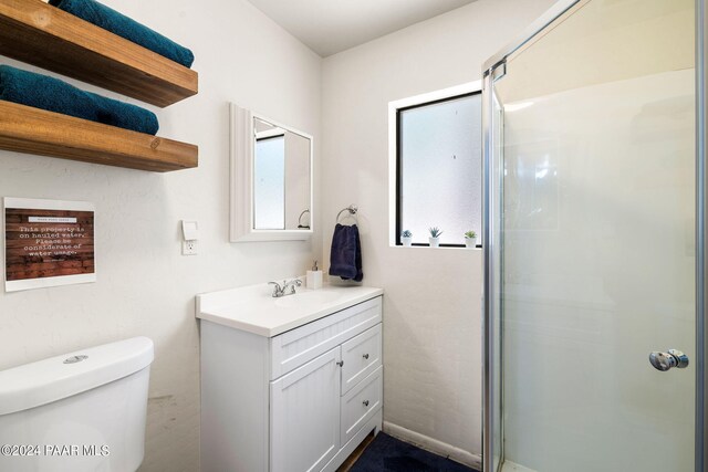 bathroom with a wealth of natural light, a shower with door, vanity, and toilet