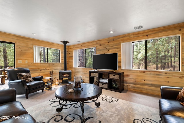 carpeted living room featuring a wood stove, wooden walls, and plenty of natural light