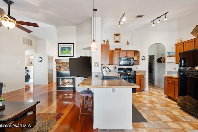 kitchen with high vaulted ceiling, decorative light fixtures, sink, a kitchen breakfast bar, and black appliances