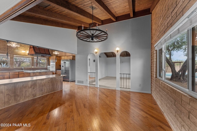 unfurnished living room with light hardwood / wood-style floors, wood ceiling, beam ceiling, and a high ceiling