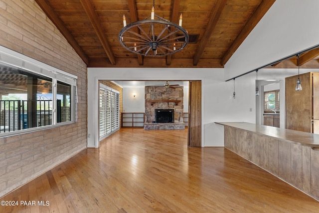 unfurnished living room featuring brick wall, wooden ceiling, vaulted ceiling with beams, light hardwood / wood-style floors, and a stone fireplace