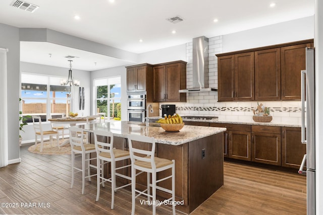 5357 Crescent Edge Dr, Prescott, AZ 86301 - kitchen featuring wall chimney range hood, stainless steel appliances, decorative backsplash, a center island with sink, and light stone countertops