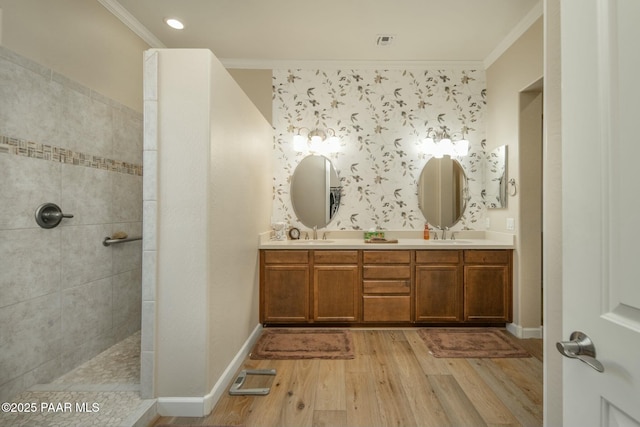 bathroom featuring wood-type flooring, vanity, a tile shower, and crown molding