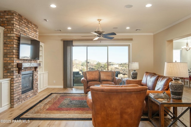 living room with a fireplace, light wood-type flooring, ceiling fan with notable chandelier, and crown molding