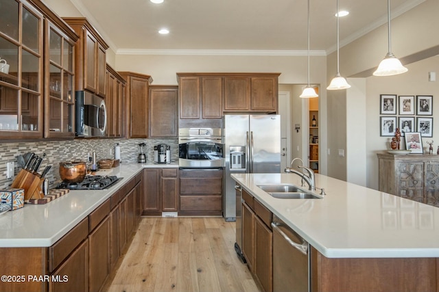 kitchen with a center island with sink, hanging light fixtures, sink, decorative backsplash, and appliances with stainless steel finishes