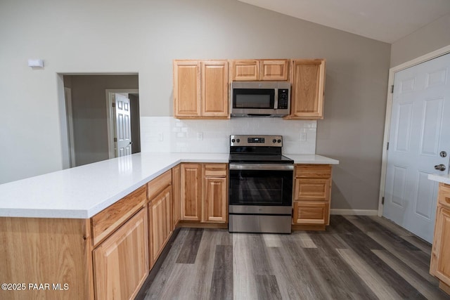 kitchen featuring vaulted ceiling, decorative backsplash, kitchen peninsula, stainless steel appliances, and dark wood-type flooring