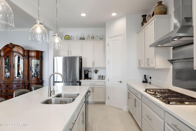 kitchen with stainless steel appliances, sink, decorative light fixtures, white cabinetry, and wall chimney range hood