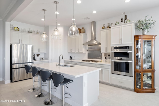 kitchen featuring wall chimney exhaust hood, decorative light fixtures, white cabinets, appliances with stainless steel finishes, and sink