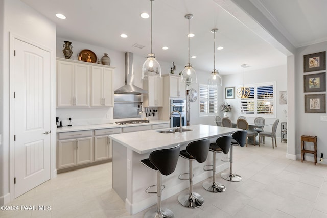 kitchen featuring sink, wall chimney exhaust hood, a breakfast bar area, a center island with sink, and pendant lighting