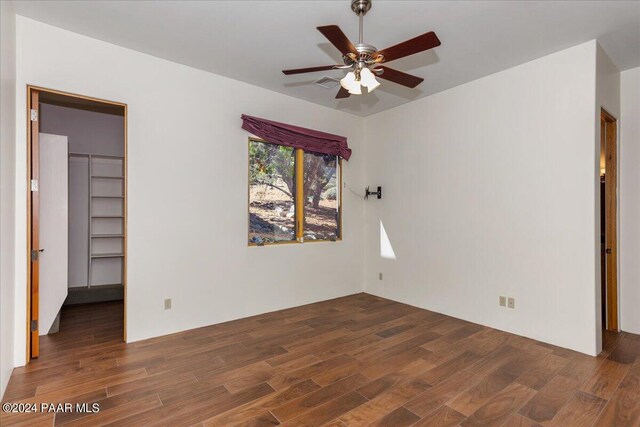 unfurnished bedroom with a spacious closet, ceiling fan, a closet, and dark wood-type flooring