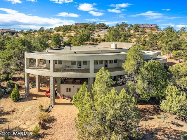 back of house with stucco siding, driveway, a patio, a balcony, and a carport