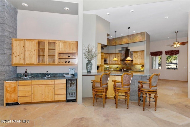 kitchen with beverage cooler, a sink, wall chimney range hood, glass insert cabinets, and a towering ceiling