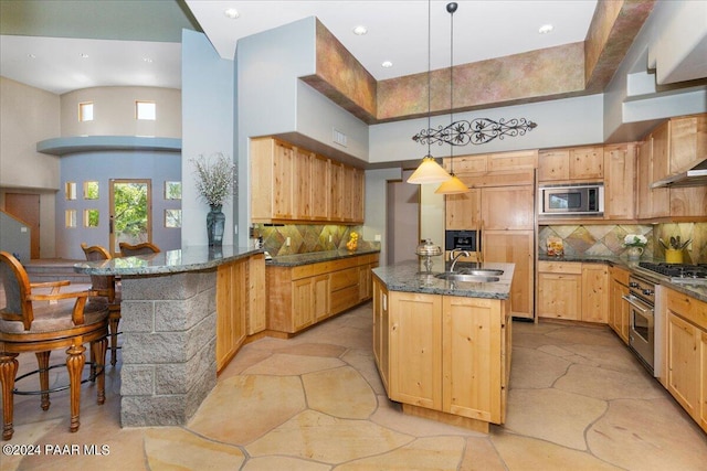 kitchen featuring backsplash, dark stone countertops, appliances with stainless steel finishes, stone tile flooring, and a sink