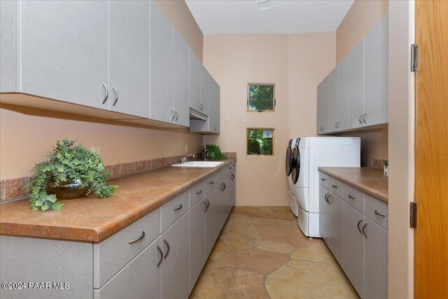 clothes washing area featuring visible vents, stone finish floor, washer and dryer, a sink, and cabinet space