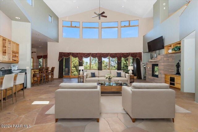 living room featuring ceiling fan, a towering ceiling, and a fireplace