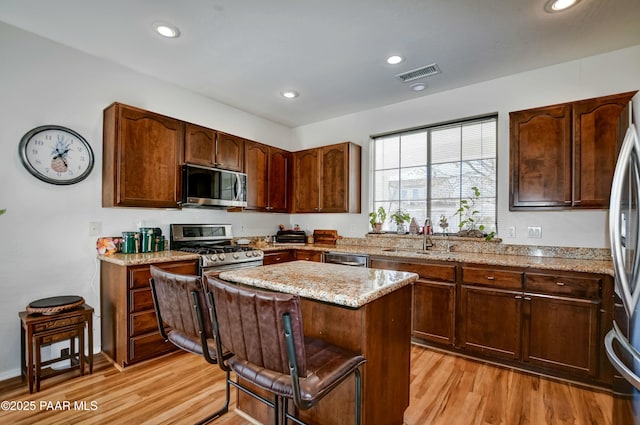 kitchen featuring sink, stainless steel appliances, a center island, light stone counters, and light hardwood / wood-style floors