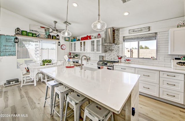 kitchen with white cabinets, a kitchen island with sink, wall chimney exhaust hood, and stainless steel gas range