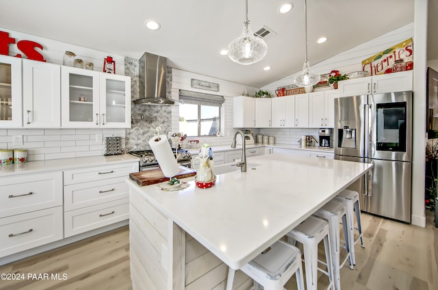 kitchen featuring a center island with sink, lofted ceiling, wall chimney range hood, and stainless steel appliances