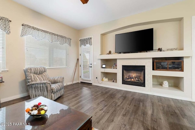 living room with wood-type flooring, built in features, and a tiled fireplace