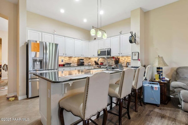 kitchen with kitchen peninsula, appliances with stainless steel finishes, a kitchen breakfast bar, pendant lighting, and white cabinetry