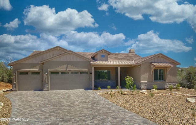 view of front of house featuring stone siding, a standing seam roof, a chimney, decorative driveway, and a garage