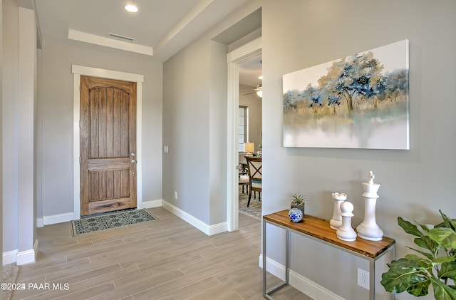 entrance foyer featuring a raised ceiling, visible vents, baseboards, light wood-type flooring, and a ceiling fan
