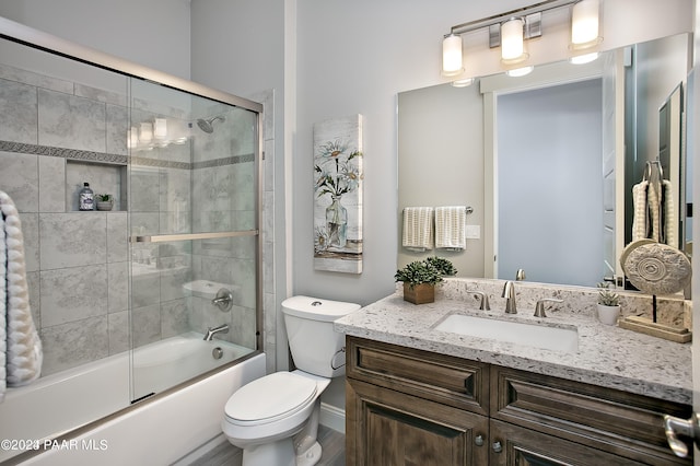 bathroom featuring shower / bath combination with glass door, baseboards, toilet, wood finished floors, and vanity
