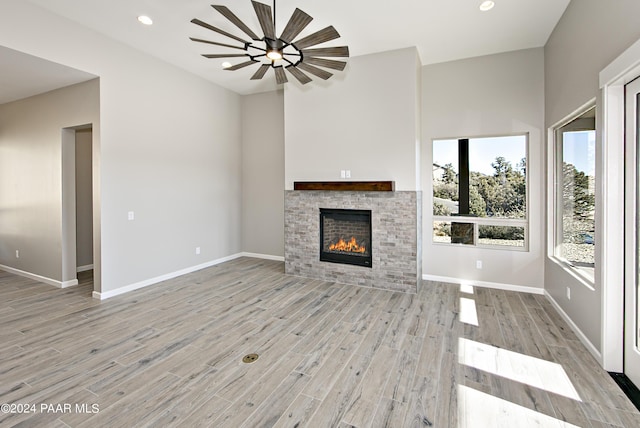 unfurnished living room with a glass covered fireplace, baseboards, recessed lighting, and light wood-style flooring