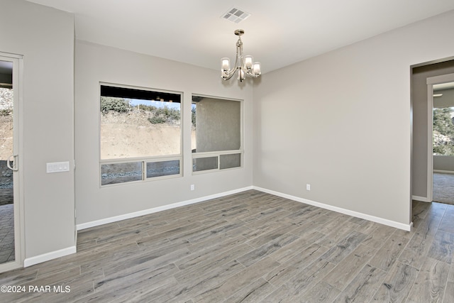 empty room with baseboards, a notable chandelier, wood finished floors, and visible vents