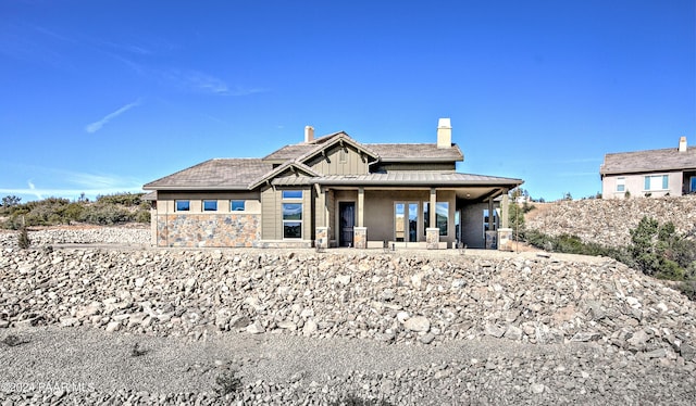 back of house with board and batten siding, a chimney, and stone siding