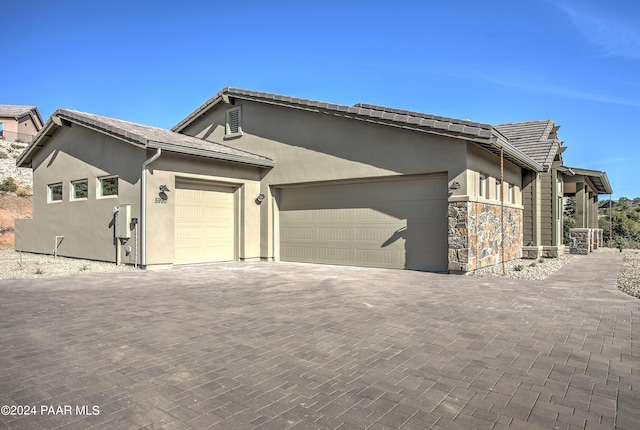 view of side of property with stucco siding, decorative driveway, a tile roof, and a garage