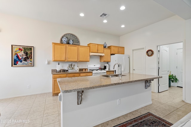 kitchen with white appliances, a sink, under cabinet range hood, light tile patterned floors, and a center island with sink