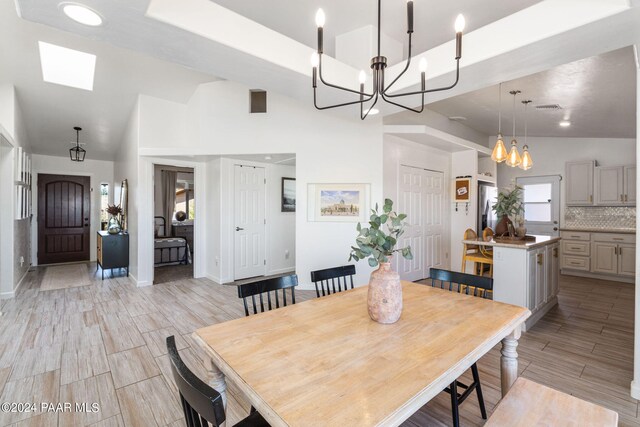 dining area with high vaulted ceiling, light hardwood / wood-style floors, an inviting chandelier, and a skylight