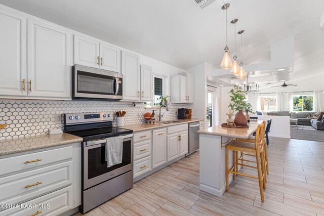 kitchen with ceiling fan, appliances with stainless steel finishes, decorative light fixtures, white cabinetry, and a breakfast bar area