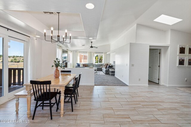 dining space with vaulted ceiling with skylight and ceiling fan with notable chandelier