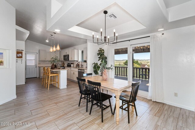 dining space with a notable chandelier, vaulted ceiling, sink, and a tray ceiling