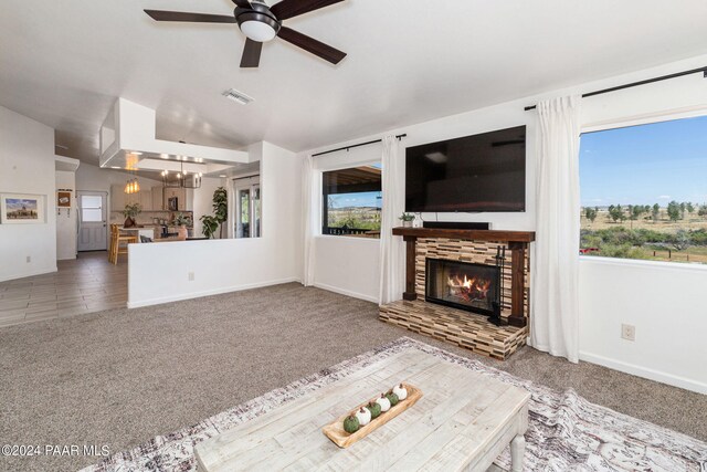 unfurnished living room featuring carpet flooring, ceiling fan with notable chandelier, a stone fireplace, and vaulted ceiling