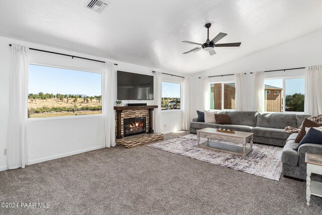 living room featuring carpet floors, vaulted ceiling, ceiling fan, and a stone fireplace