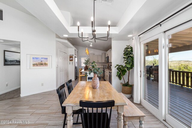 dining space with a raised ceiling, light hardwood / wood-style flooring, vaulted ceiling, and a notable chandelier