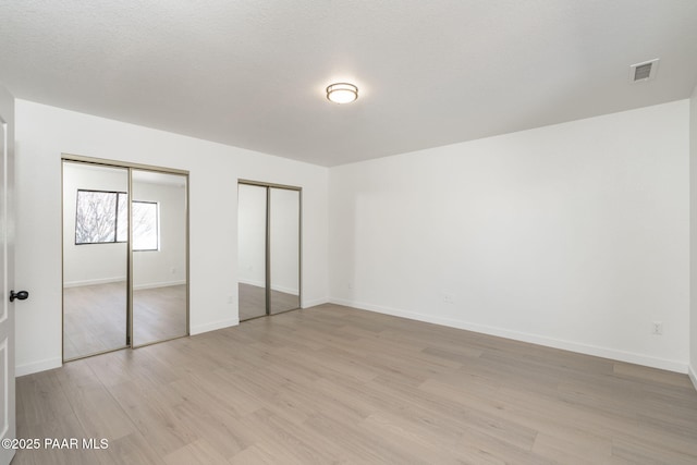 unfurnished bedroom featuring multiple closets, a textured ceiling, and light wood-type flooring