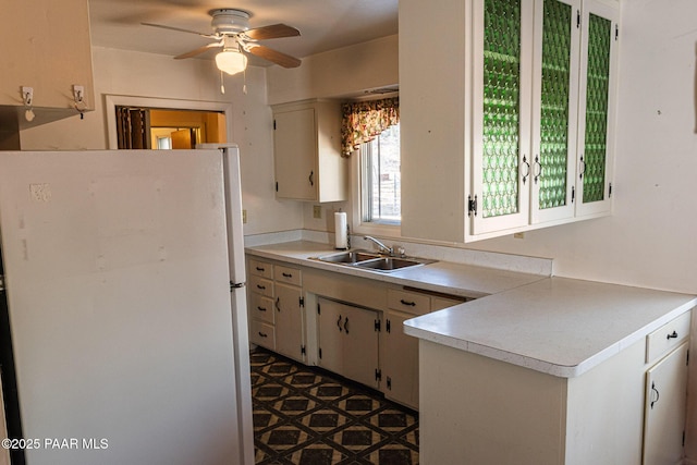 kitchen featuring light countertops, a ceiling fan, freestanding refrigerator, and a sink