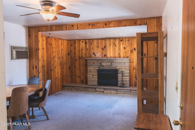 carpeted office with a stone fireplace, wood walls, ceiling fan, and a wall unit AC