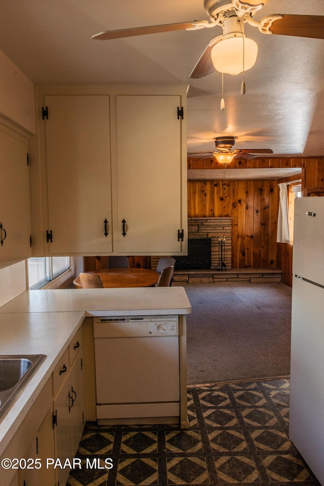 kitchen featuring white appliances, a ceiling fan, a fireplace with raised hearth, wood walls, and dark carpet