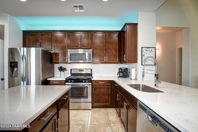 kitchen with sink, appliances with stainless steel finishes, light tile patterned flooring, light stone counters, and dark brown cabinetry